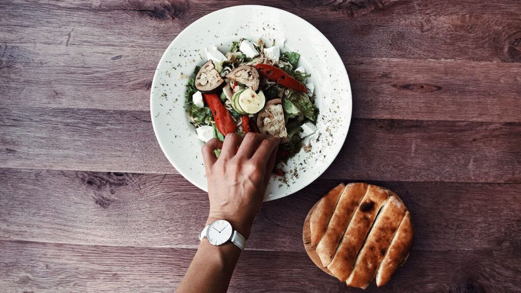 close-up of hand with watch on wrist reaching for a plate of vegetables
